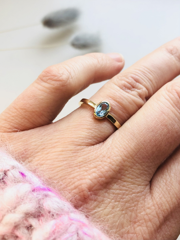 Guldring med oval lyseblå sten på hånd