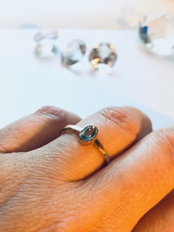 Guldring med oval lyseblå sten på finger